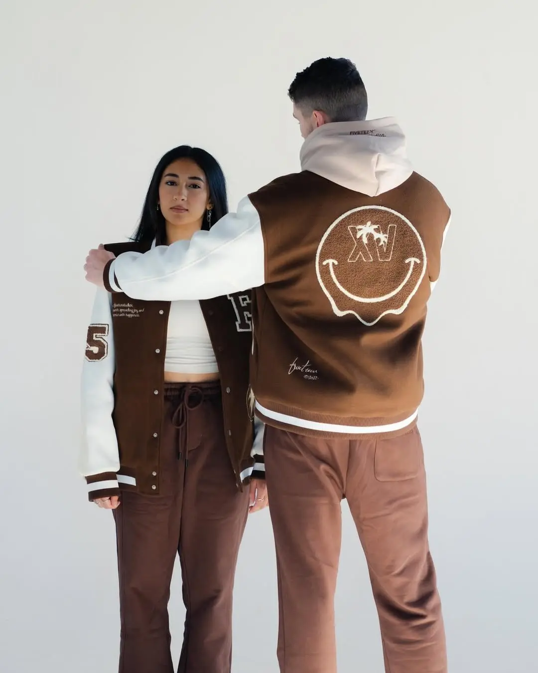 Couple in mocha varsity jackets with cream sleeves and matching brown pants