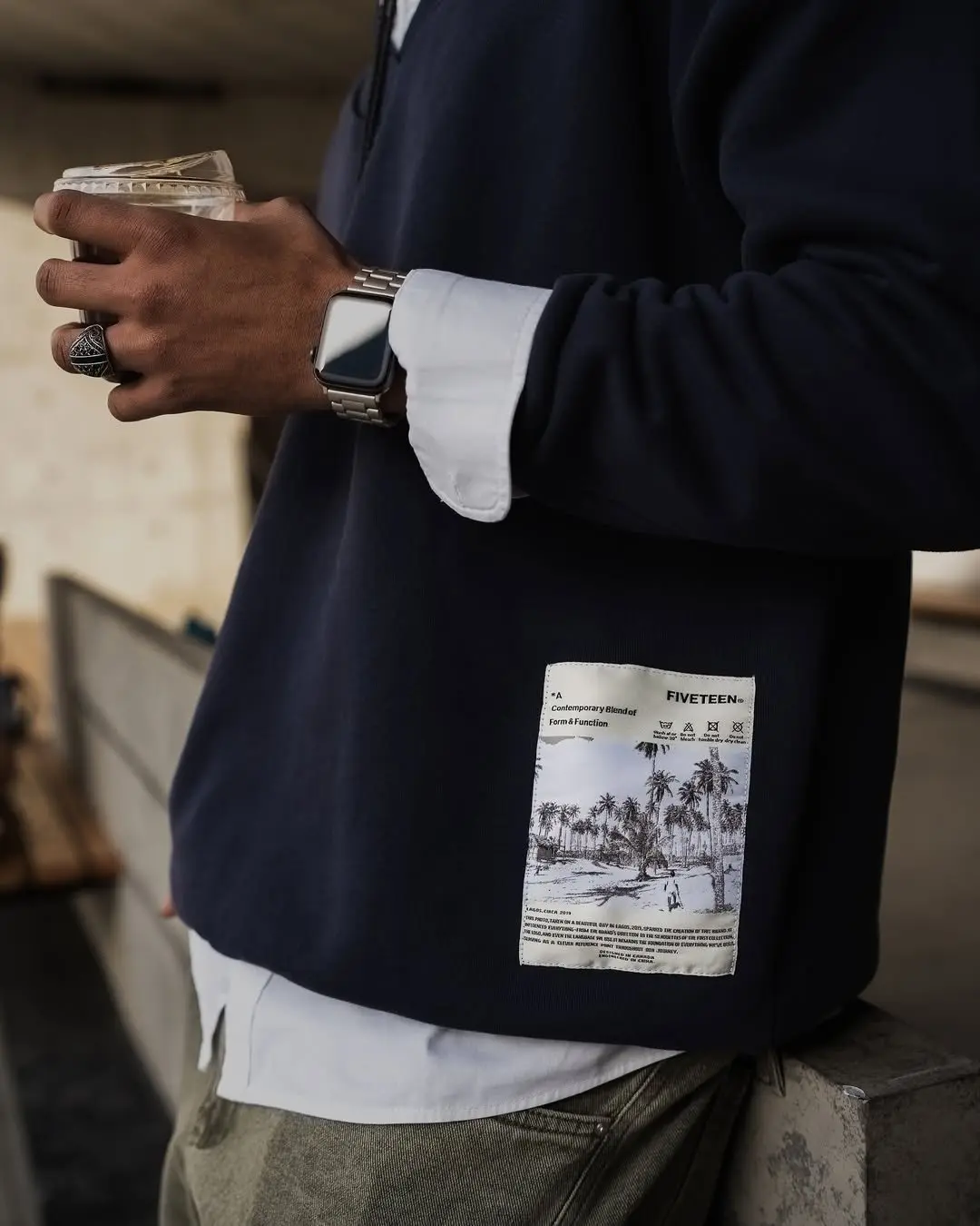 Close-up of a navy crewneck with a printed palm postcard patch