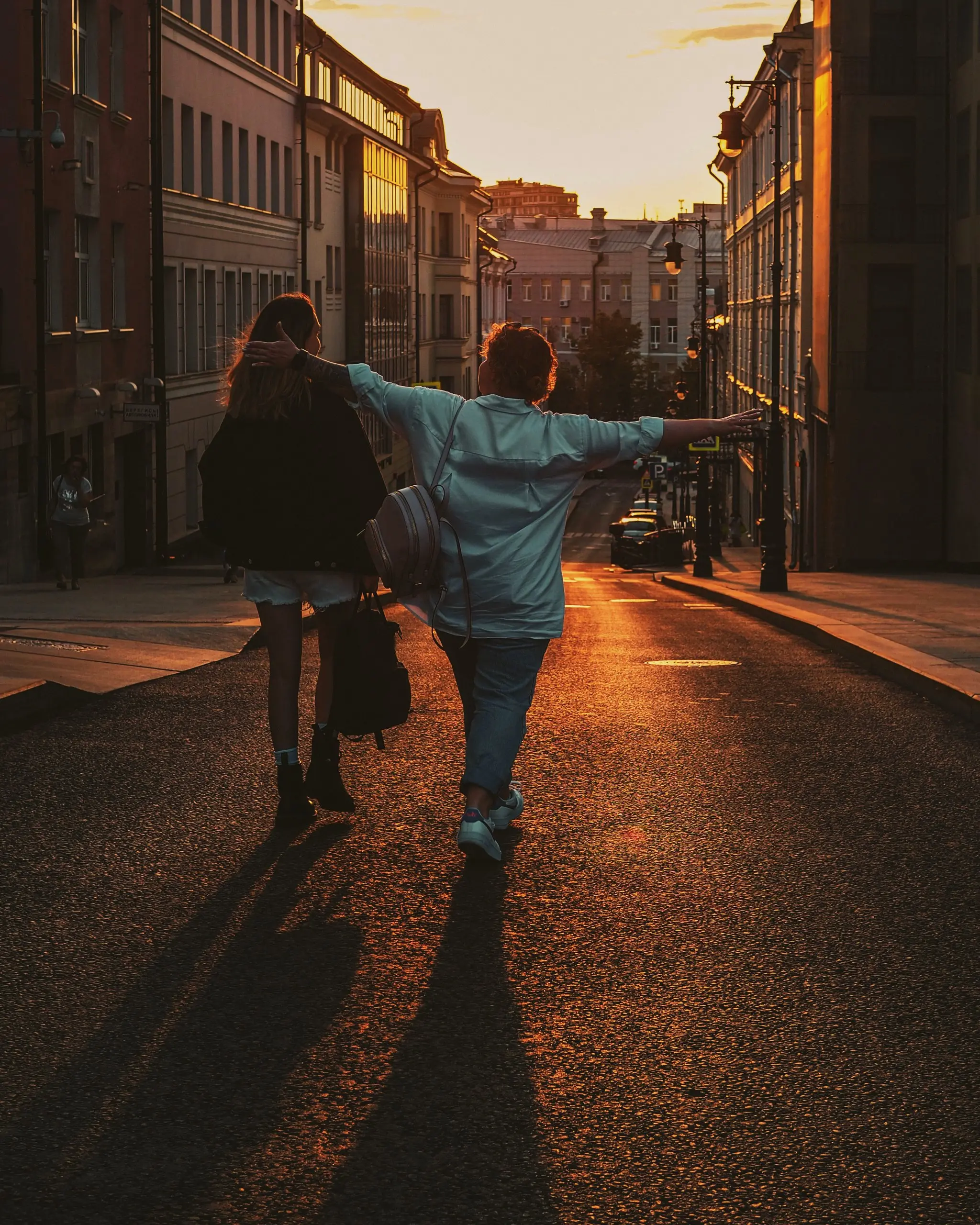 Pale blue overshirt and black jacket on two friends walking down a city street at golden hour, long shadows